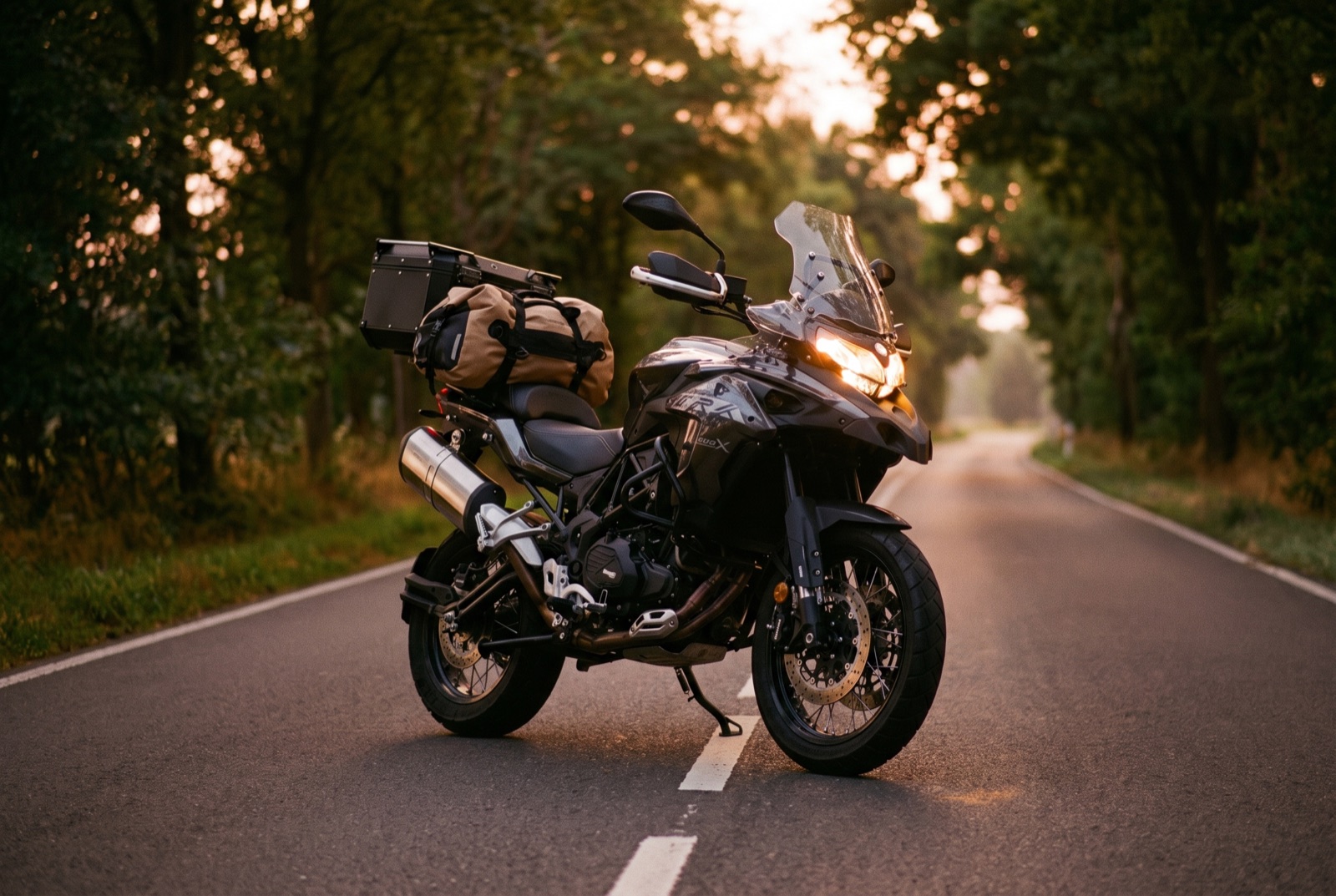 Anthrazitfarbene Benelli TRK 502X mit leuchtendem Scheinwerfer auf einer dämmrigen Landstraße
